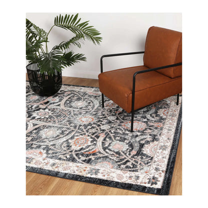 Estate Charcoal traditional rug styled with a tan leather chair and potted plant, showing its large floral pattern