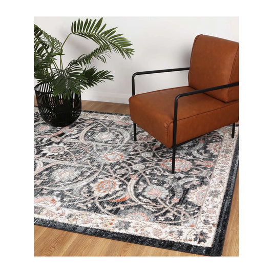 Estate Charcoal traditional rug styled with a tan leather chair and potted plant, showing its large floral pattern