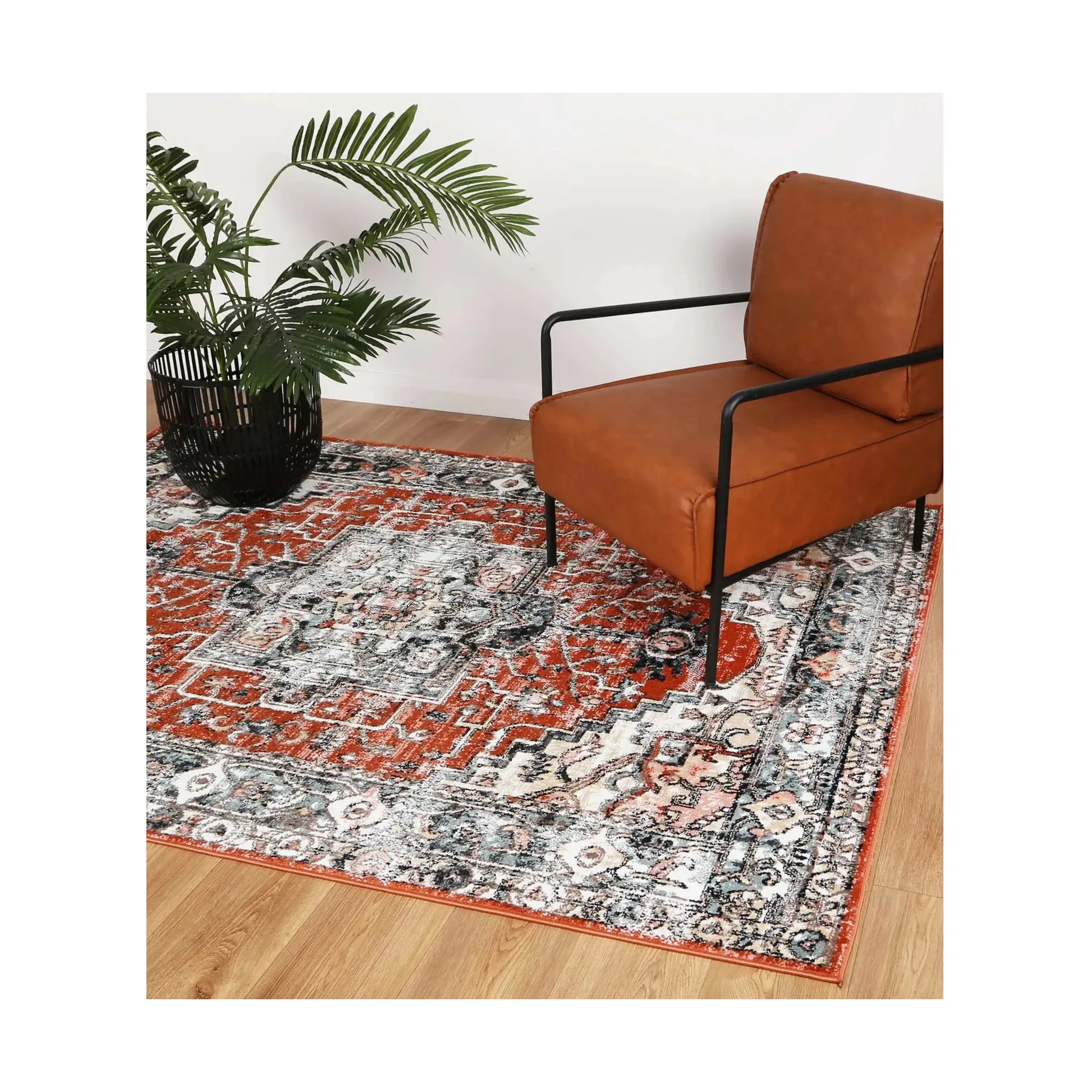 Estate Terracotta medallion rug styled with a leather chair and plant, showing its terracotta, ivory and charcoal pattern