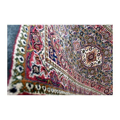 Angled close-up of Fine Bidjar rug showing the red floral border, pale guard bands and ivory medallion beyond