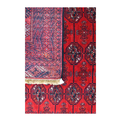 Close-up of a folded corner showing the Tekke rug’s reverse weave beside its red gül field and pale fringe