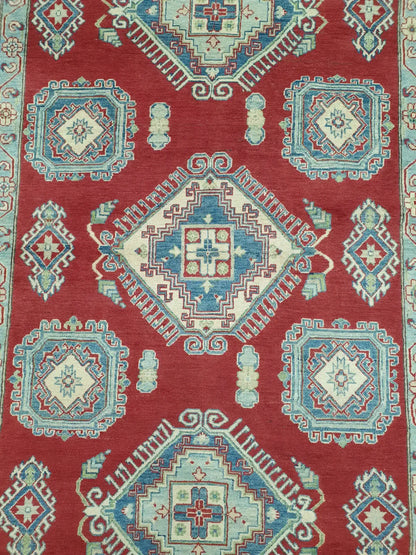 Top-down view of a hand-knotted Kazak wool rug showcasing its central geometric medallions in red, cream, and blue tones.