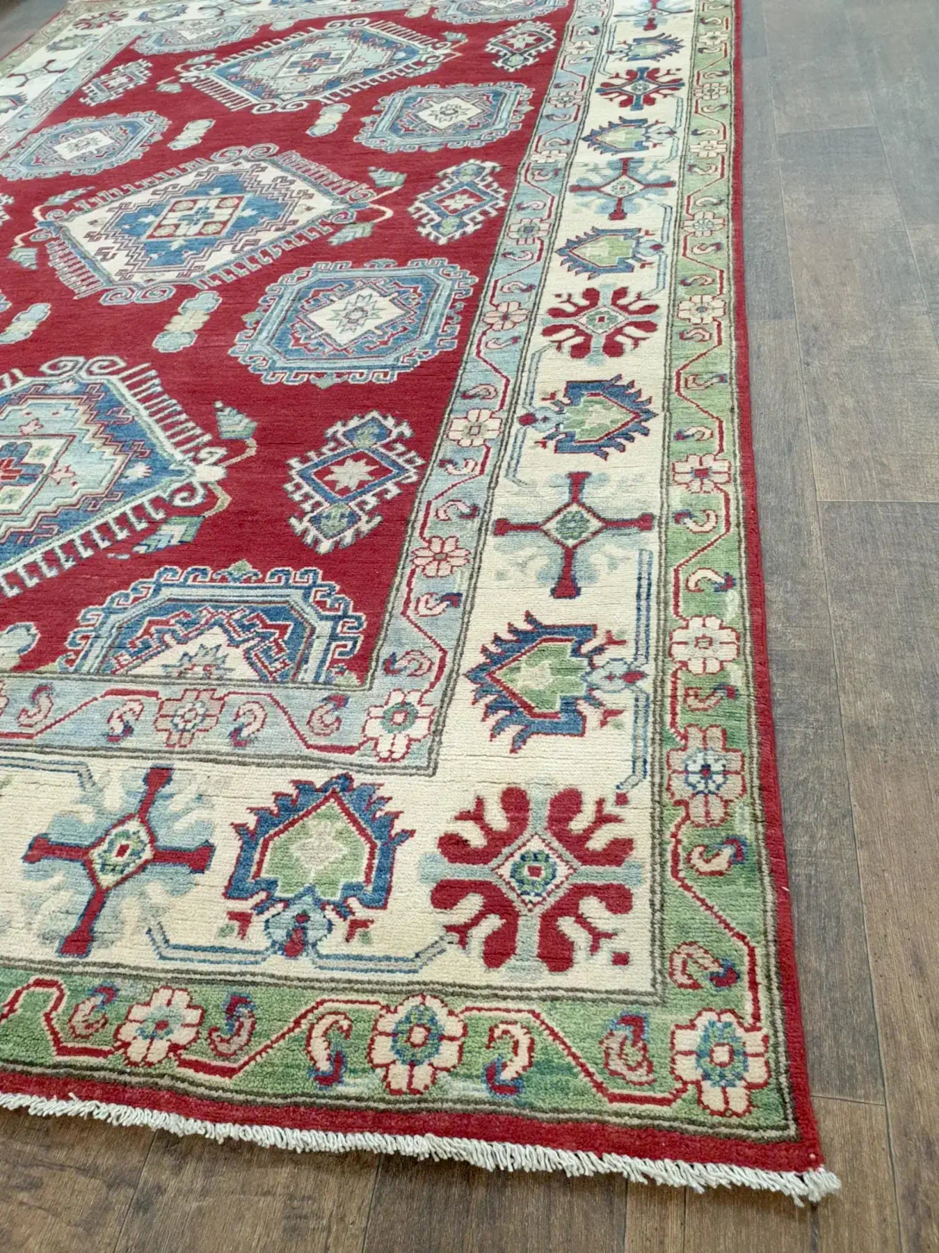 Close-up of red Kazak wool rug showing cream geometric weave and dense pile