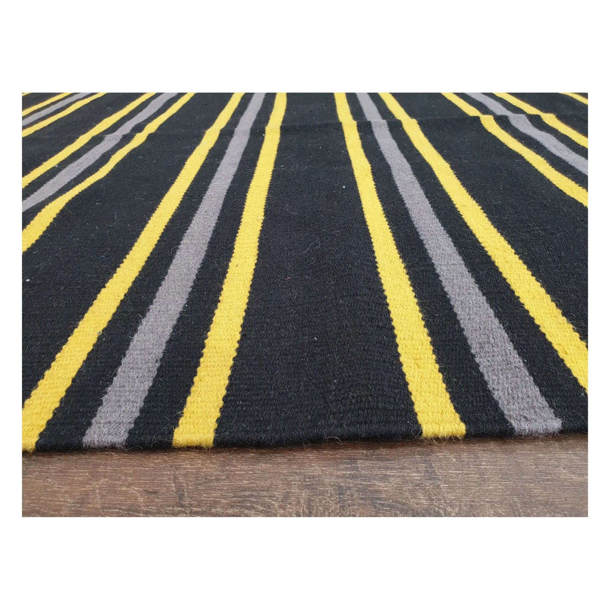 Low-angle close-up of Indian Dhurrie fine wool rug showing striped flatweave texture in charcoal, yellow, and grey, 230 x 160 cm