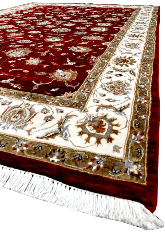 Angled view of Indian Ziegler rug showing its red floral field, ivory patterned border and white fringe