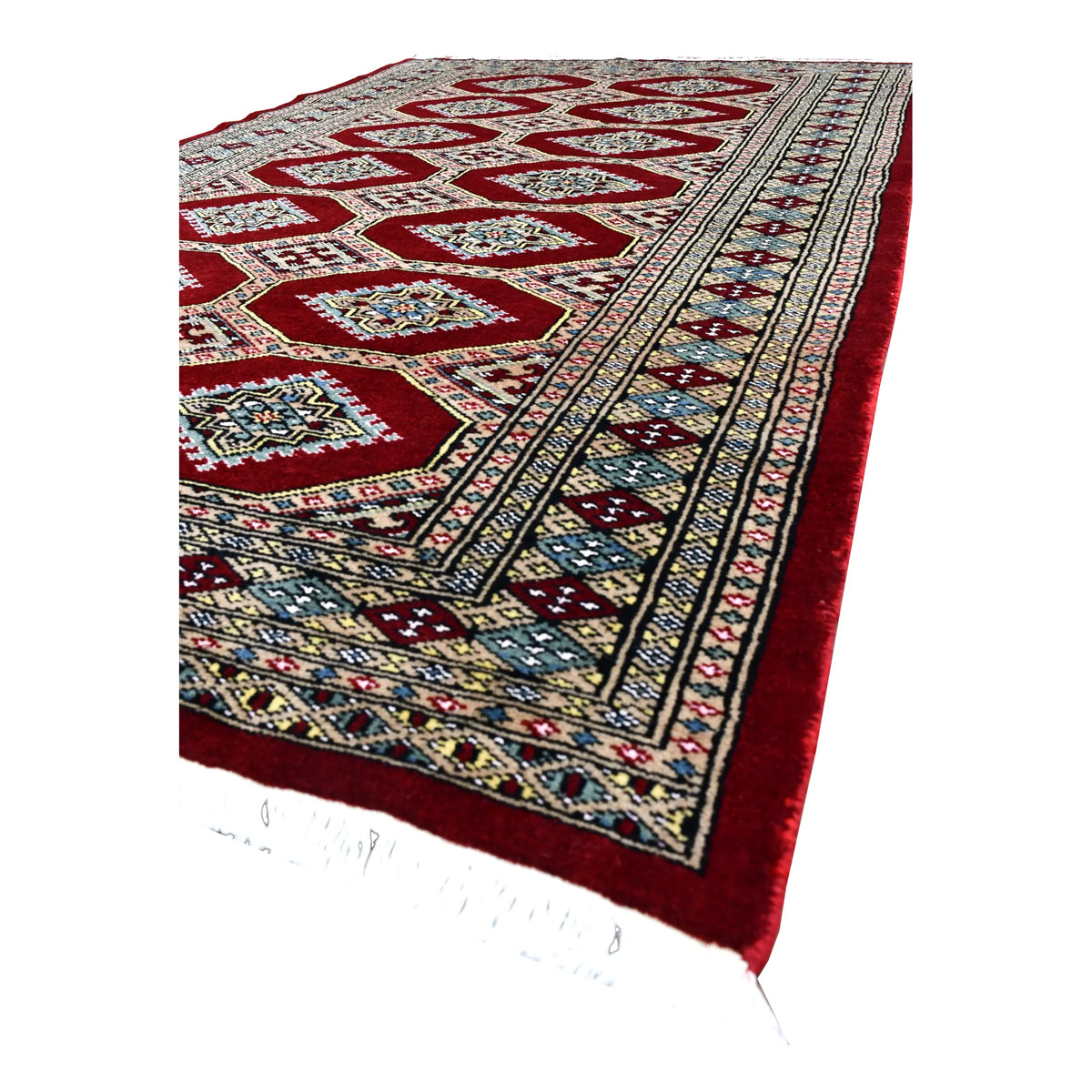 Angled view of Jaldar wool rug showing its deep red gul field, layered beige and blue borders and pale fringe