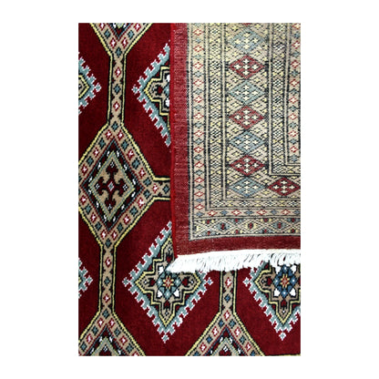 Folded-corner detail of Jaldar rug showing the reverse weave, deep red patterned front and pale fringe