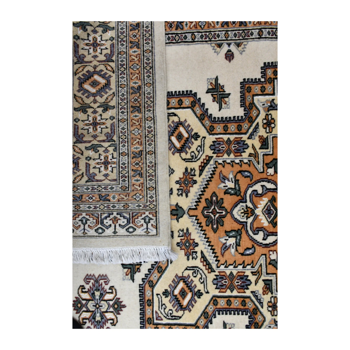 Folded-corner detail of Jaldar wool rug showing the muted reverse weave beside its warm beige medallion field and white fringe