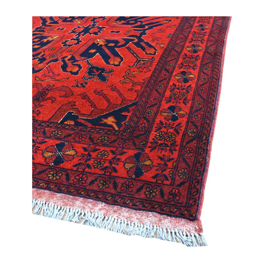 Angled view of Khal Mohammadi wool rug showing its red field, navy geometric medallion, patterned borders and pale fringe