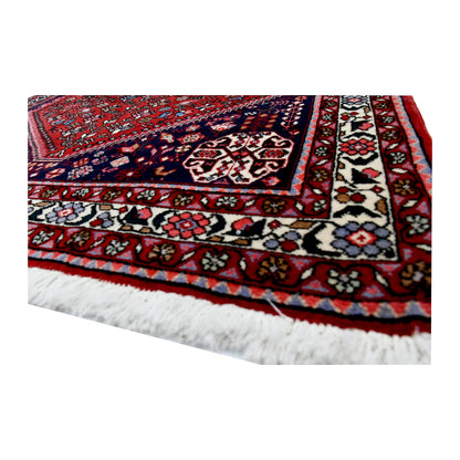 Angled corner and fringe view of Persian Abadeh wool rug showing border detail, red field and light fringe