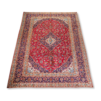 Angled full view of Persian Kashan wool rug showing red medallion field, ornate border and hand-knotted pile