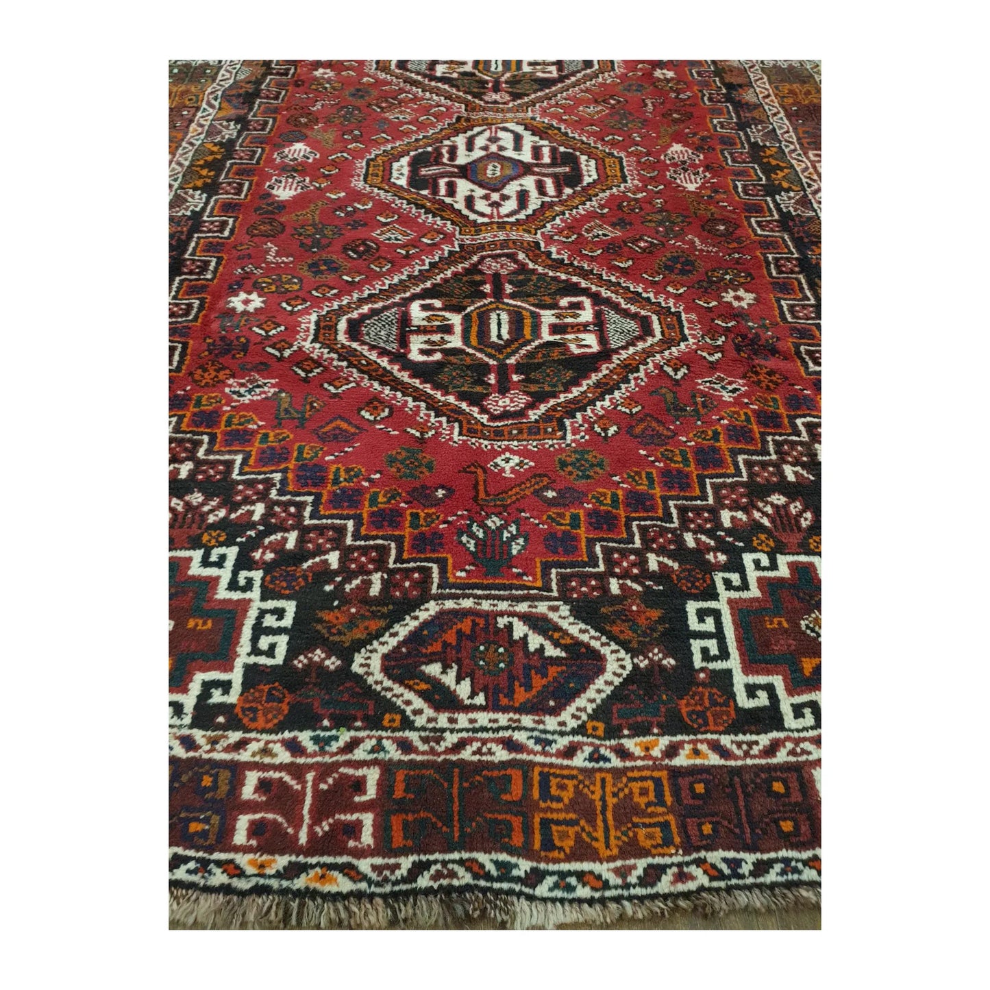 Close-up of Persian Shiraz rug showing the lower field, geometric medallion, patterned end border and visible fringe