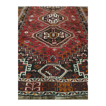 Close-up of Persian Shiraz rug showing the lower field, geometric medallion, patterned end border and visible fringe