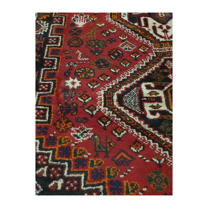 Close-up of Persian Shiraz rug showing a geometric medallion edge, red field motifs and stepped side border