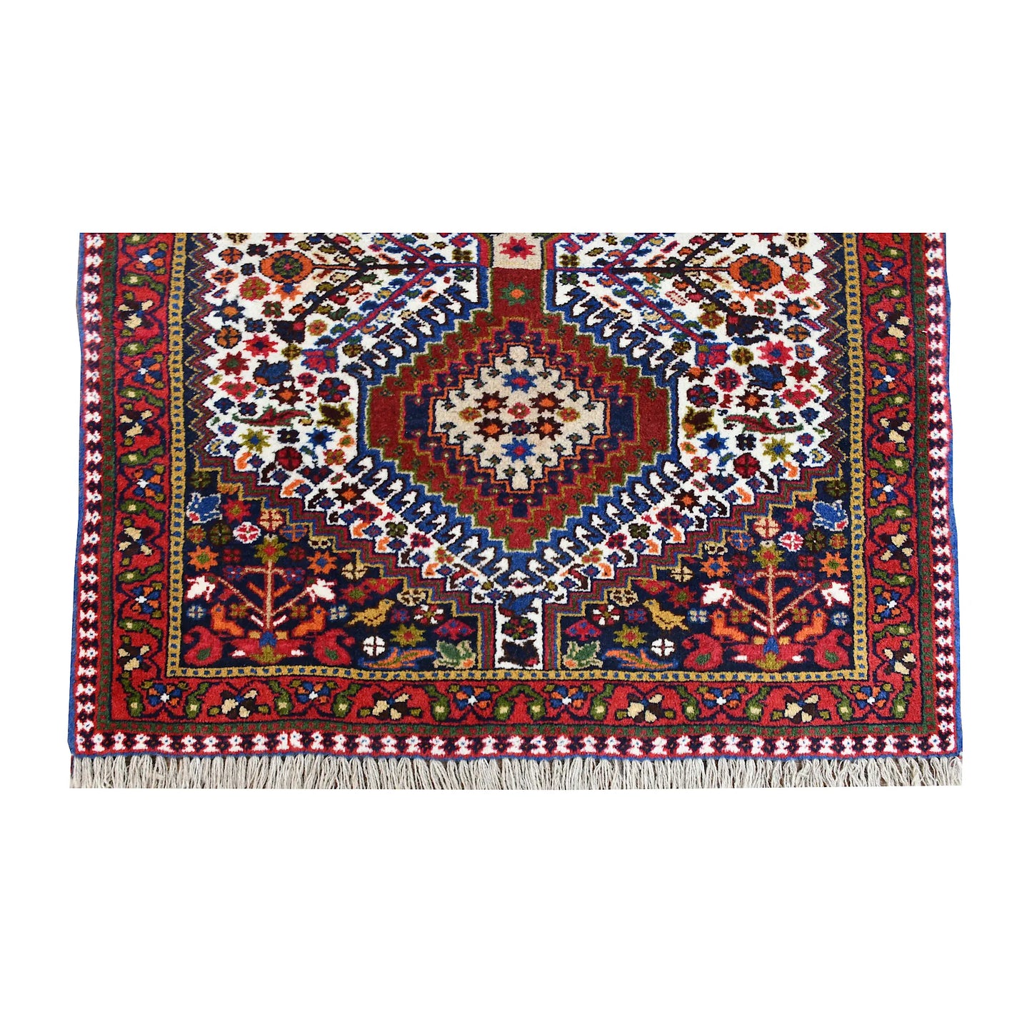 End view of Persian Yalameh rug showing a hooked diamond medallion, red corner panels and fringe
