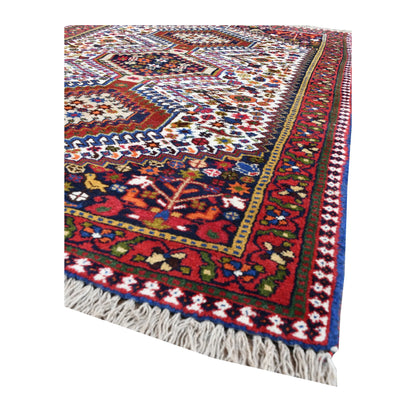 Angled corner of Persian Yalameh rug showing the layered red border, ivory field and fringe