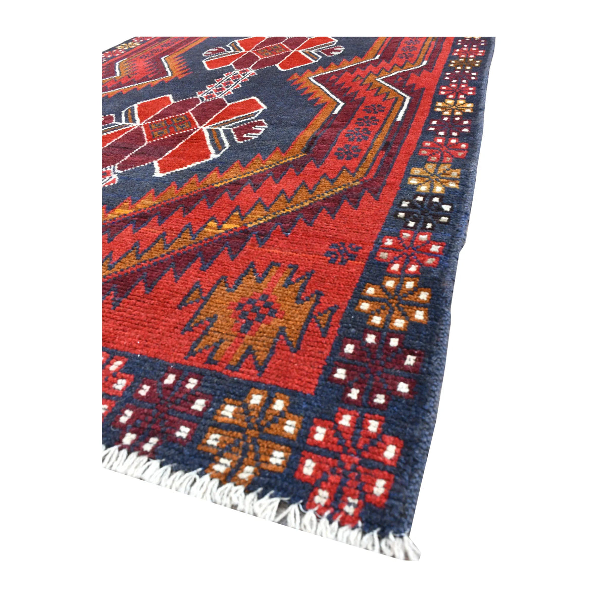 Angled view of red Baluchi wool rug showing its geometric field, patterned border and pale fringe