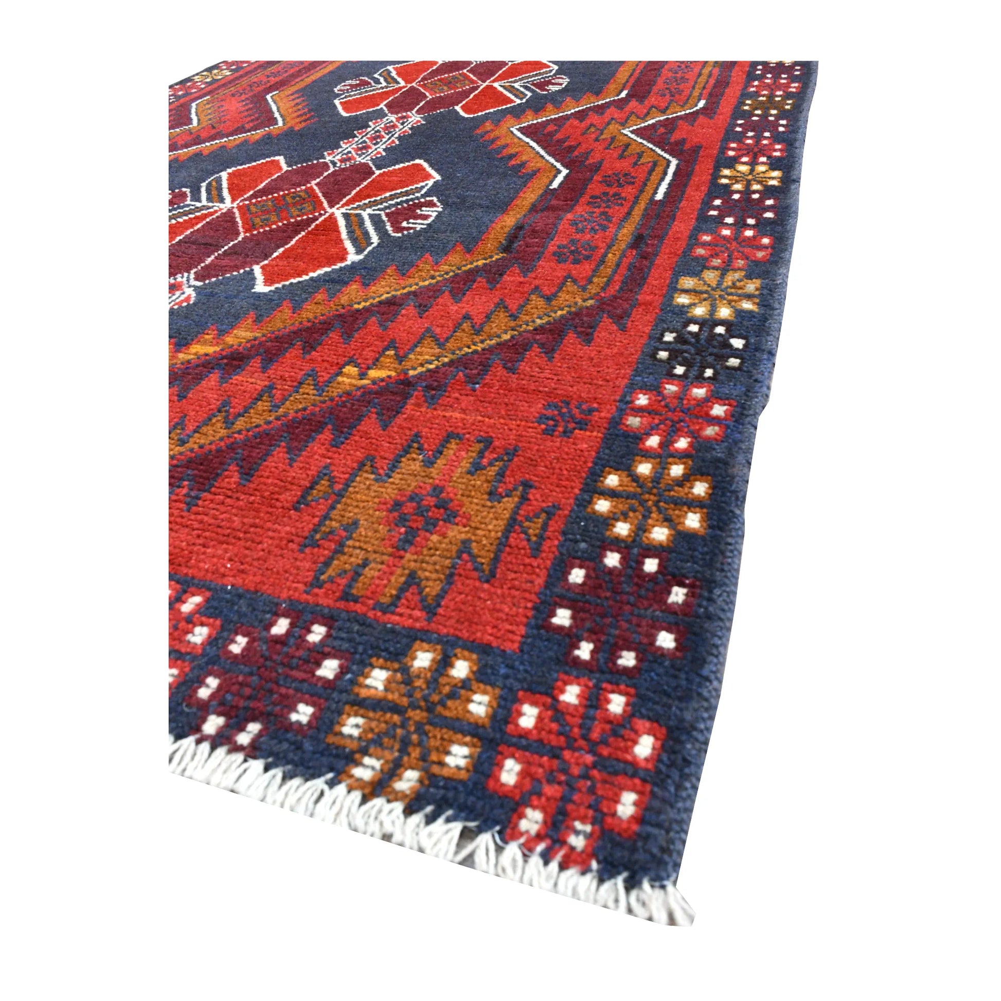 Angled view of red Baluchi wool rug showing its geometric field, patterned border and pale fringe