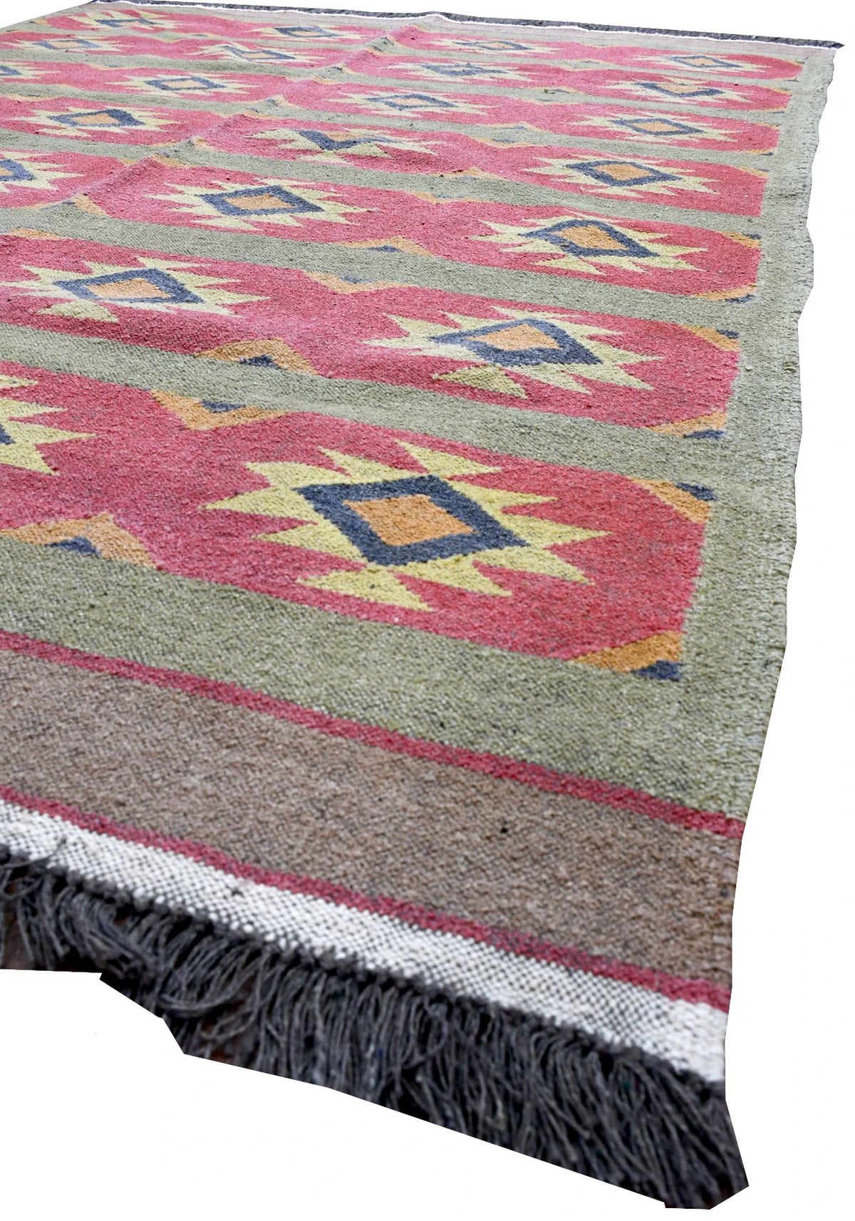 Angled detail of Turkish kilim showing pink geometric bands, plain borders, a cream end strip and charcoal fringe