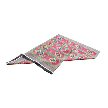 Turkish kilim with corners turned back, showing the pink and sage-green pattern, plain borders and fringed ends