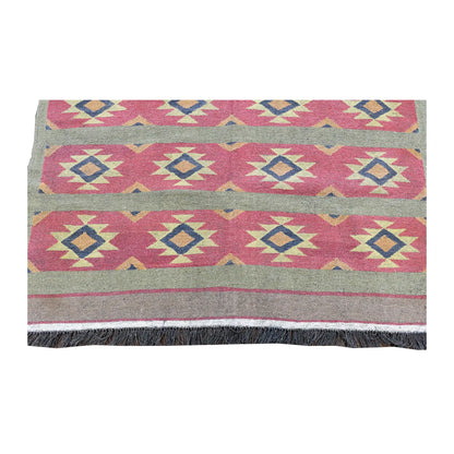 Fringe-end view of Turkish kilim with repeating stars and diamonds across pink bands above the plain end border