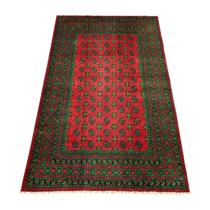 Angled full view of Afghan Turkoman wool rug showing its red gul field and layered green and navy borders