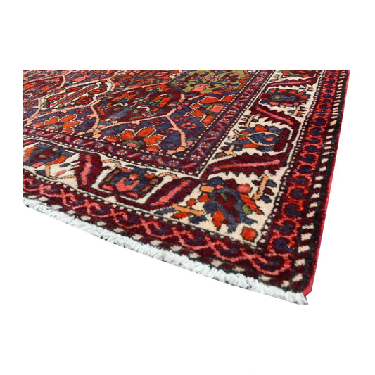 Angled corner of vintage Bakhtiari rug showing cream fringe, ivory floral border and richly coloured garden-panel field