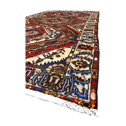 Angled view of Persian Bakhtiari rug showing its layered diamond design, ivory patterned border and white fringe