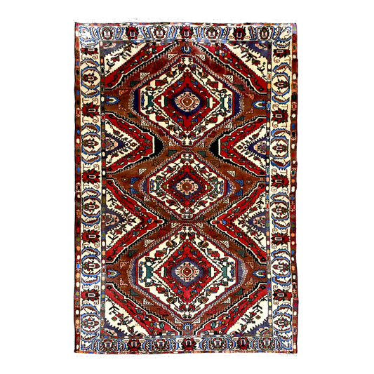 Full view of vintage Persian Bakhtiari wool rug with three diamond medallions, rust-red chevrons and ivory floral border, 287 x 155 cm