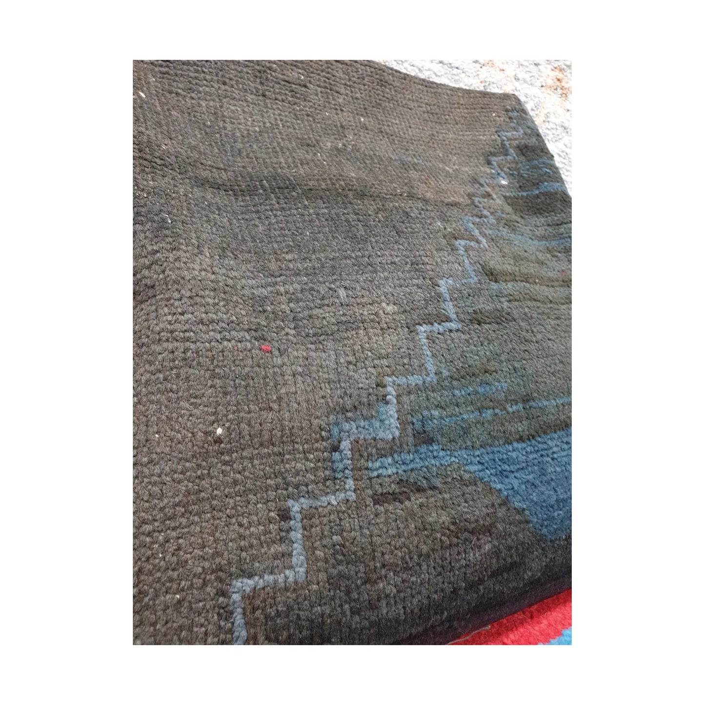 Angled close-up of dark charcoal wool pile and muted blue stepped lines on the Persian cushion cover