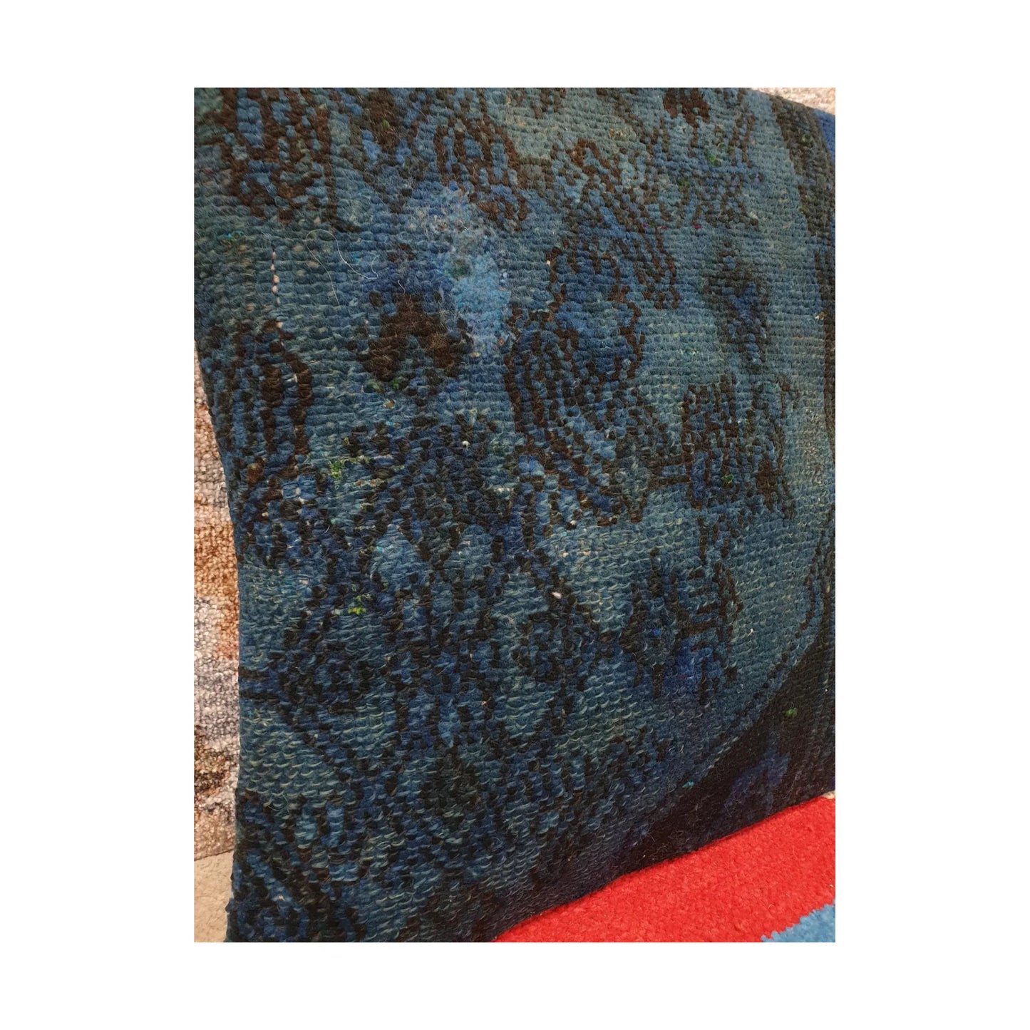 Angled close view of layered blue wool pile, fragmented floral pattern and dark piping on the Persian cushion cover