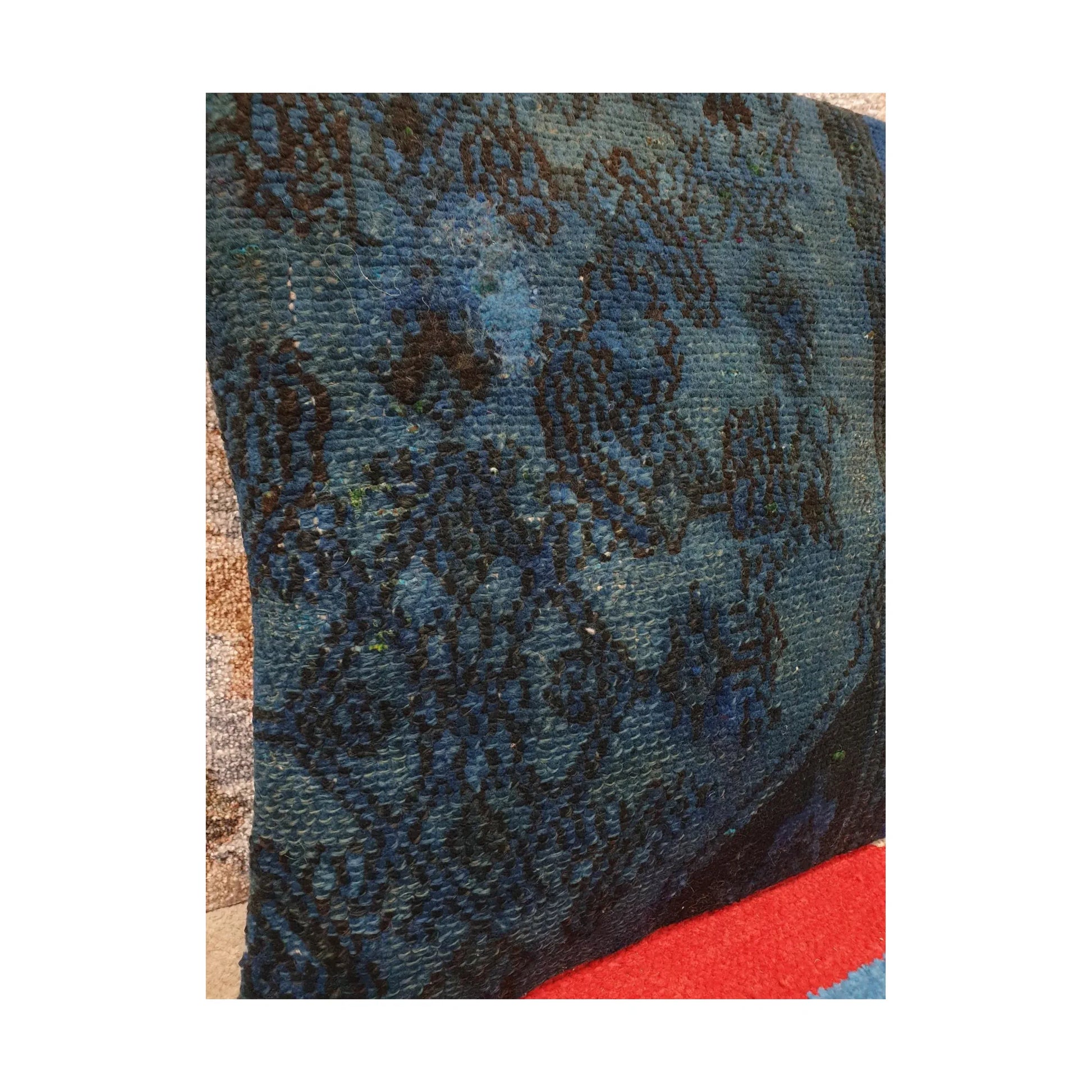 Angled close view of layered blue wool pile, fragmented floral pattern and dark piping on the Persian cushion cover