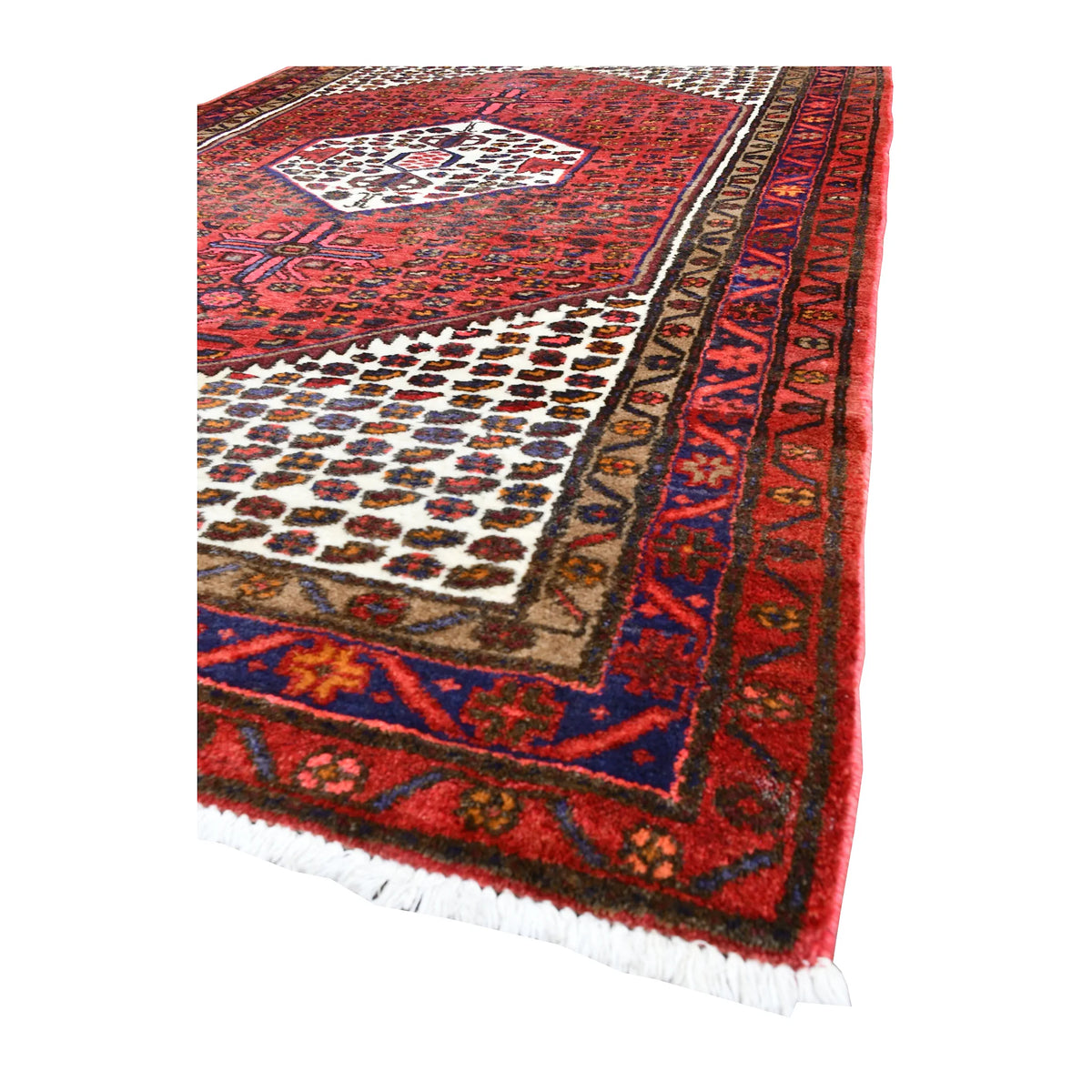 Angled view of vintage Persian Hamadan wool rug showing its red field, cream spandrels, layered border and pale fringe