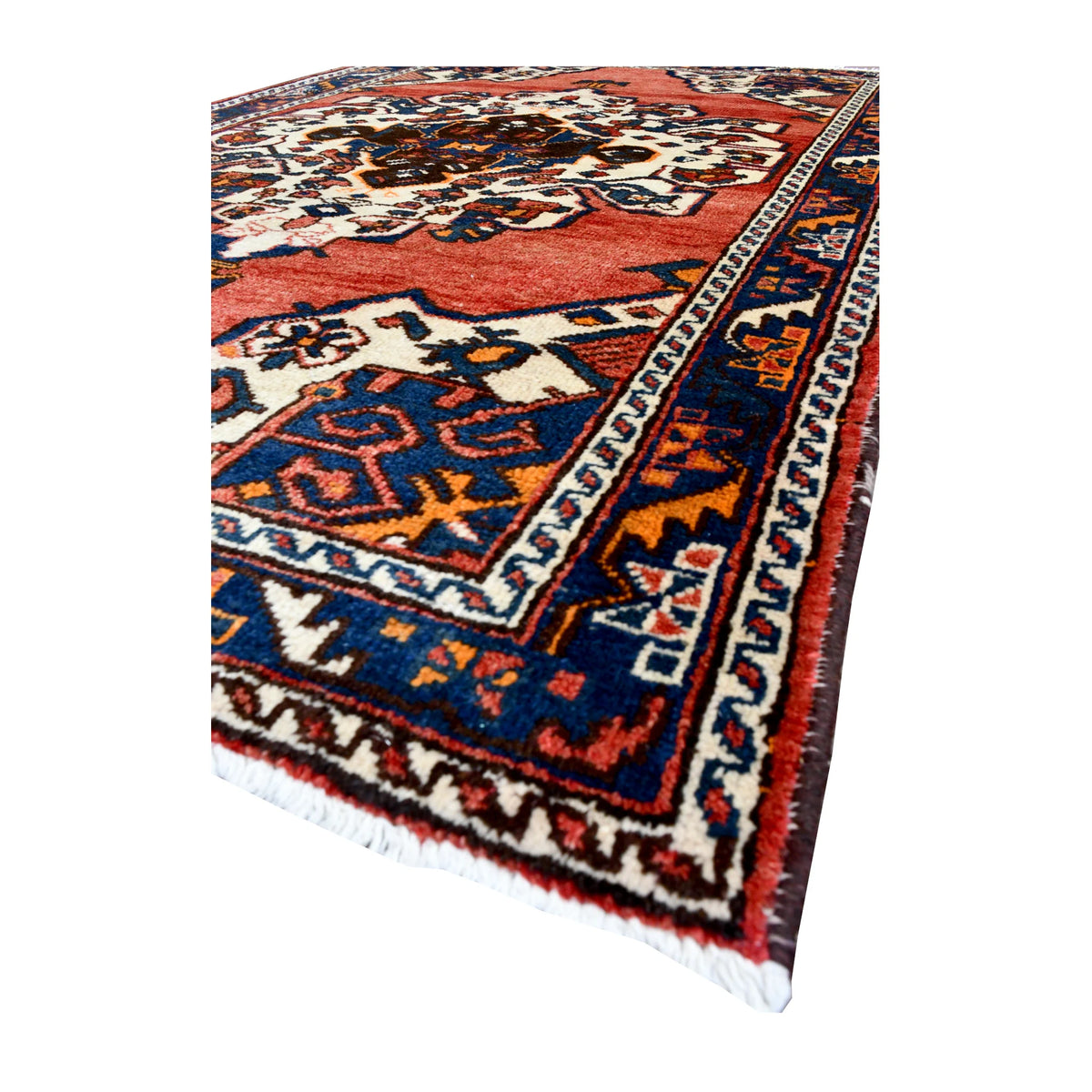 Angled view of vintage Persian Hamadan wool rug showing its central medallion, layered border and pale fringe