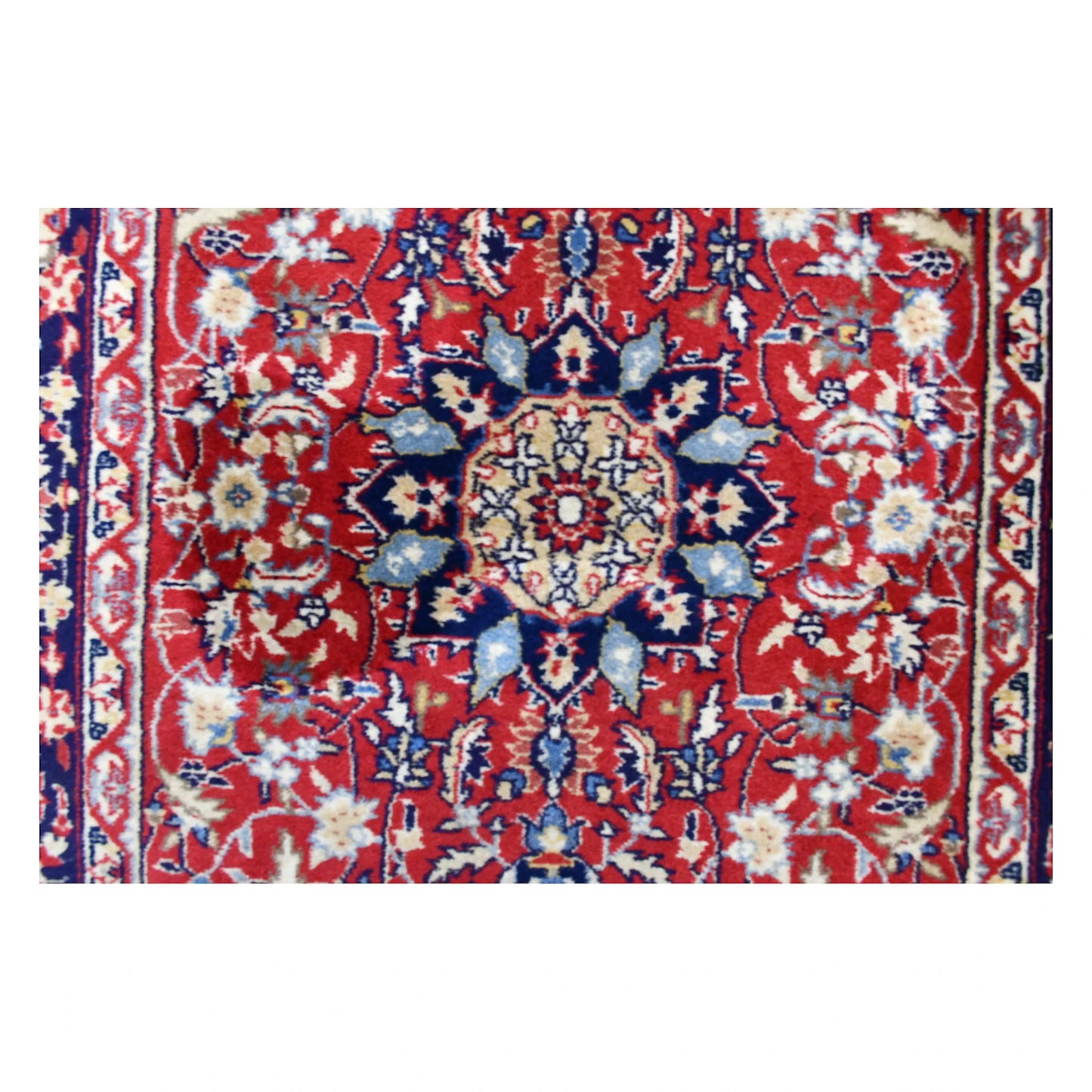 Detailed view of a blue, ivory and pale-blue floral medallion surrounded by curling vines on the red Kashan field