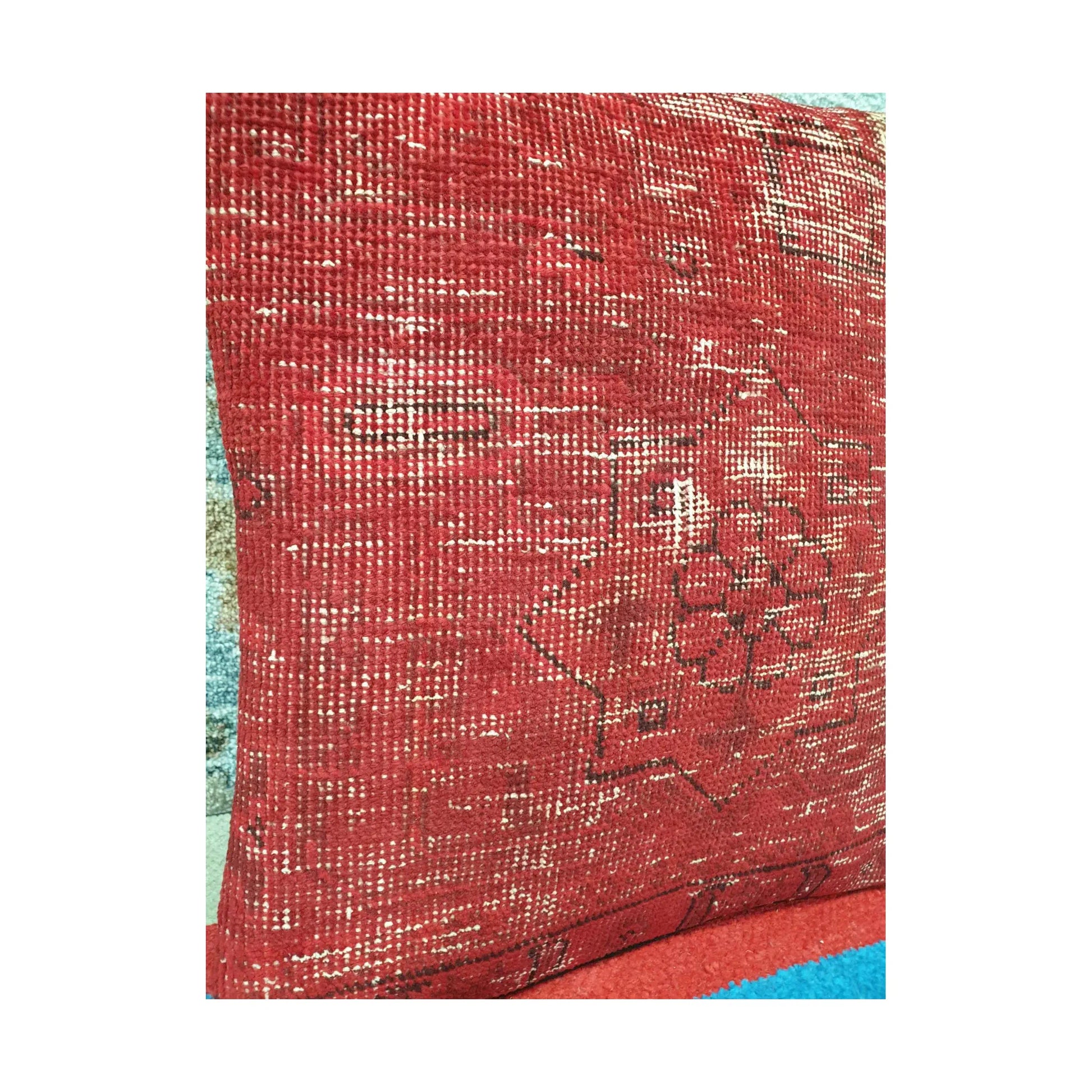Angled view of softened red wool pile with faded ivory lines and dark Persian pattern fragments