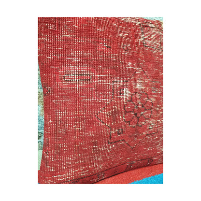 Angled view of softened red wool pile with faded ivory lines and dark Persian pattern fragments
