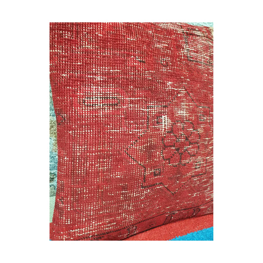 Angled view of softened red wool pile with faded ivory lines and dark Persian pattern fragments