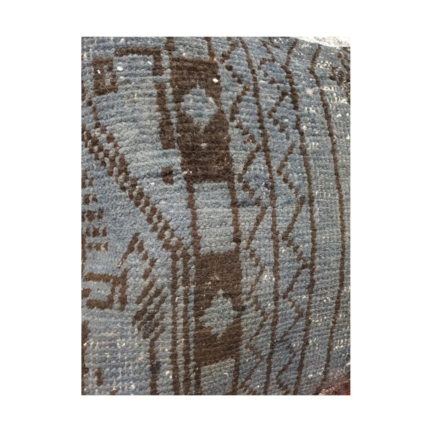 Close-up of dark brown geometric forms and linear border bands across the slate blue wool pile
