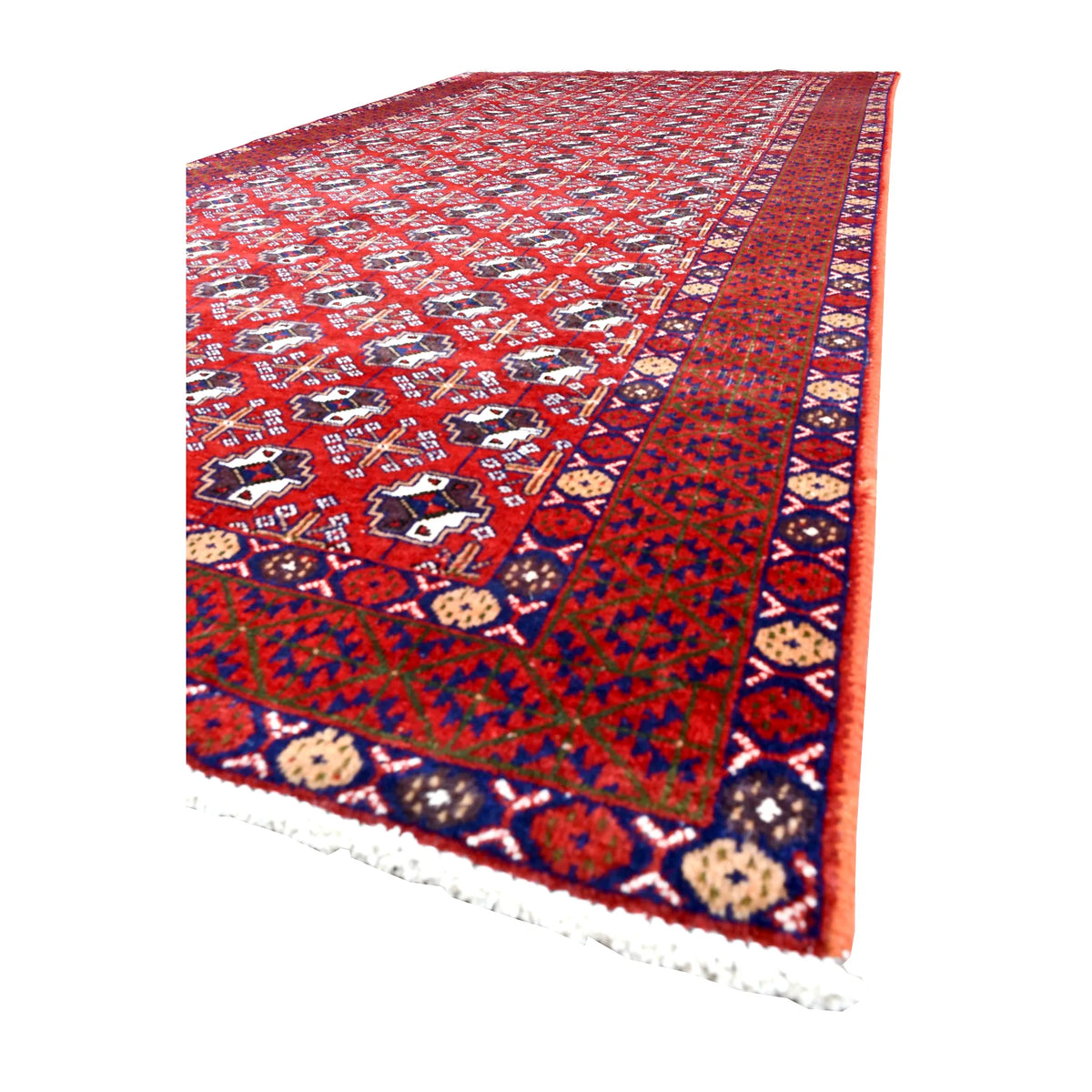 Angled view of Persian Turkoman wool rug showing its red gul field, dark geometric borders, dense pile and pale fringe