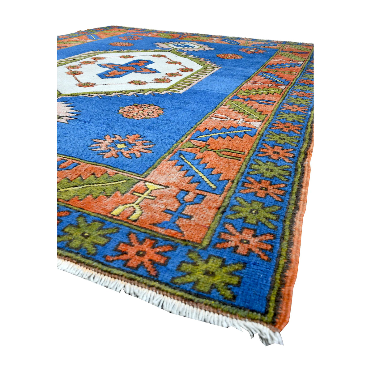 Angled view of vintage Turkish Anatolian wool rug showing its cobalt-blue field, ivory medallion, colourful borders and pale fringe