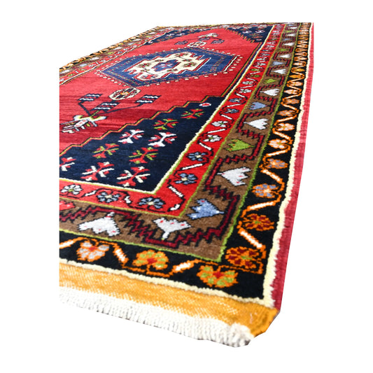 Angled view of Turkish Yahyali rug showing its red field, navy medallion, colourful geometric border and white fringe