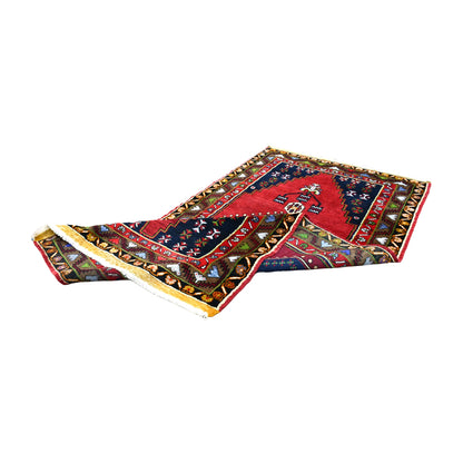 Folded view of Turkish Yahyali wool rug showing its red and navy geometric front, patterned border and reverse